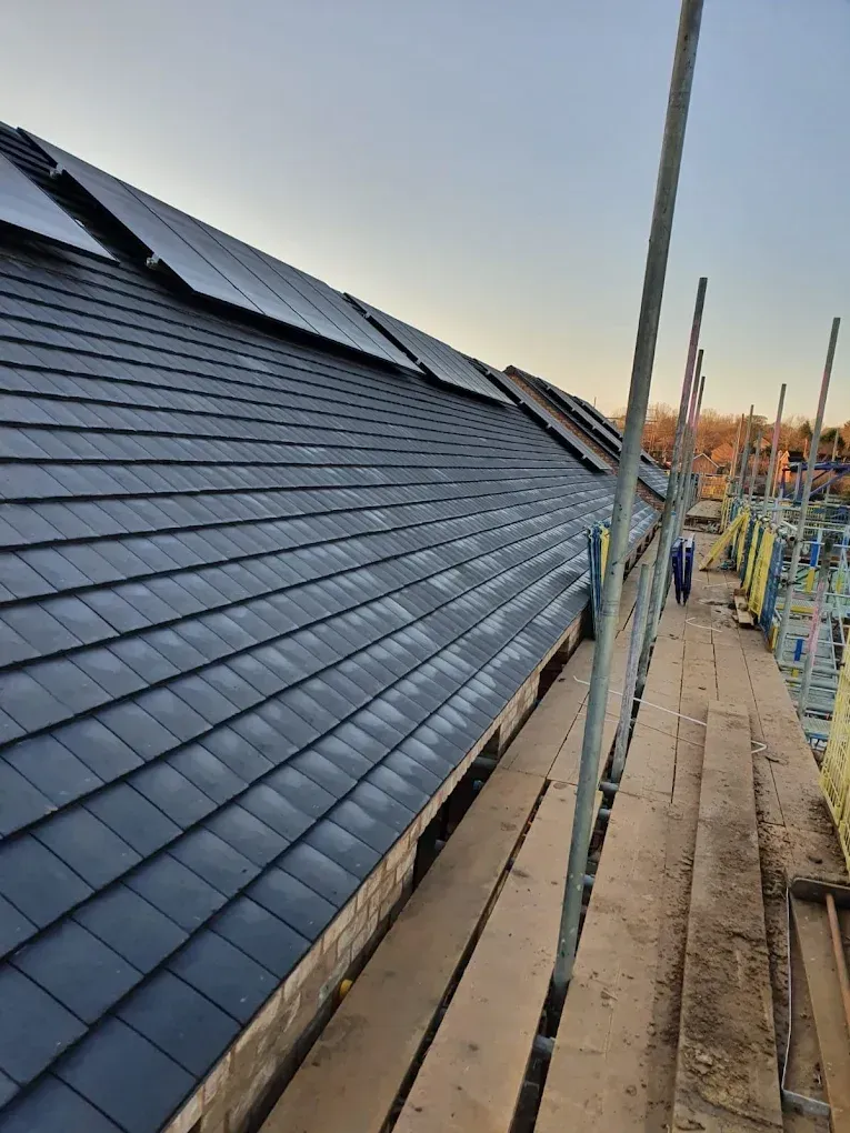 New-build terrace roof in dark grey tiles with solar panels along the top, seen from the scaffold