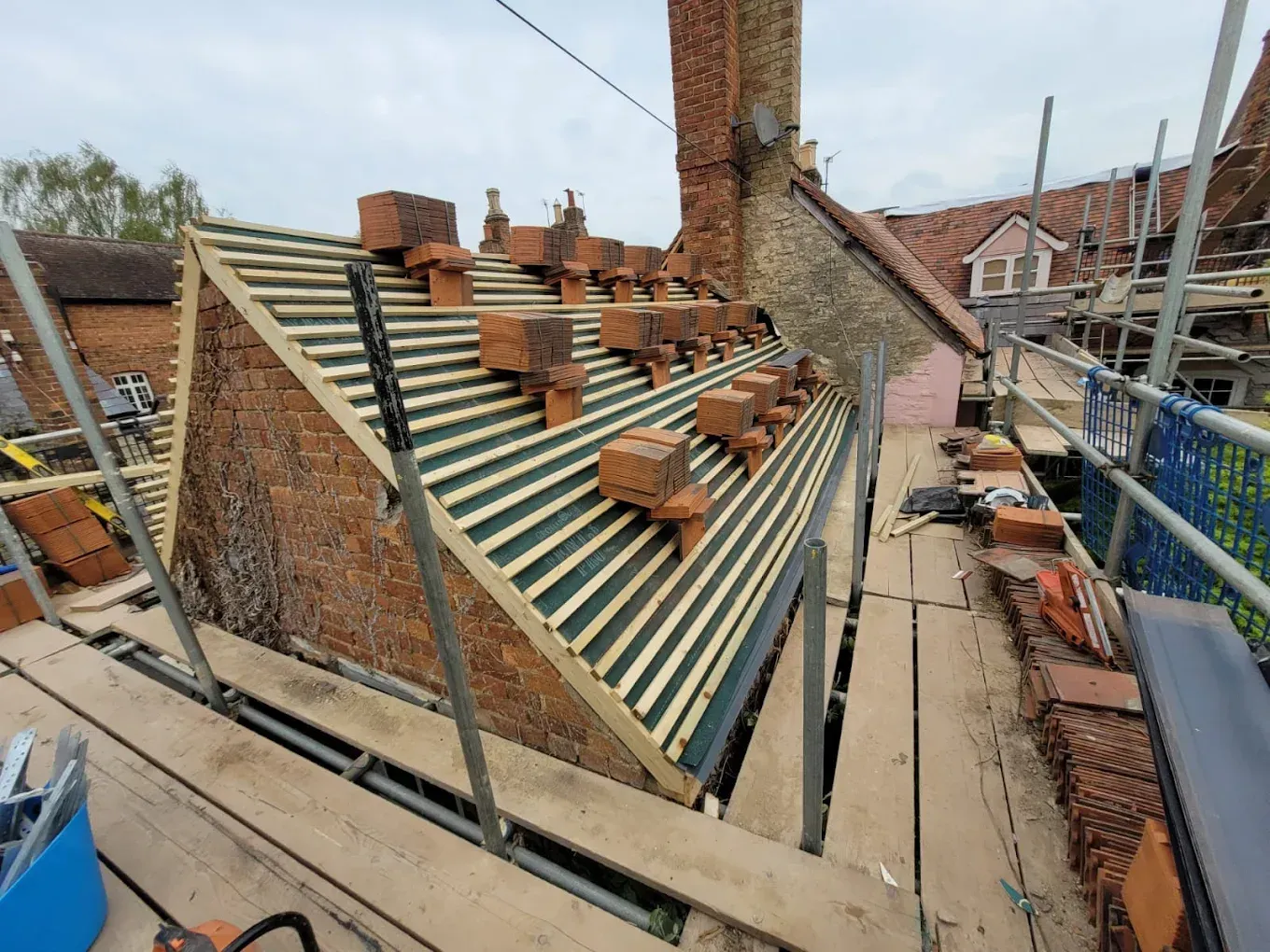 Re-roof in progress on an old brick house: new breathable membrane and battens, with clay tiles loaded out on the roof ready to lay